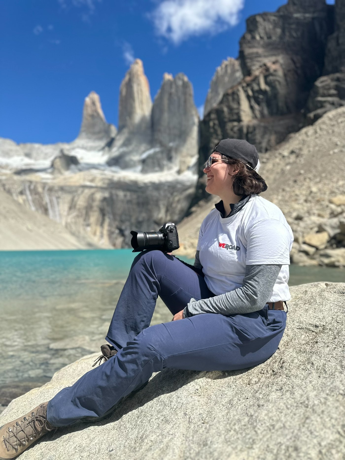 Janet sitzt mit ihrer Kamera vor einem Bergsee und markanten Felsspitzen.