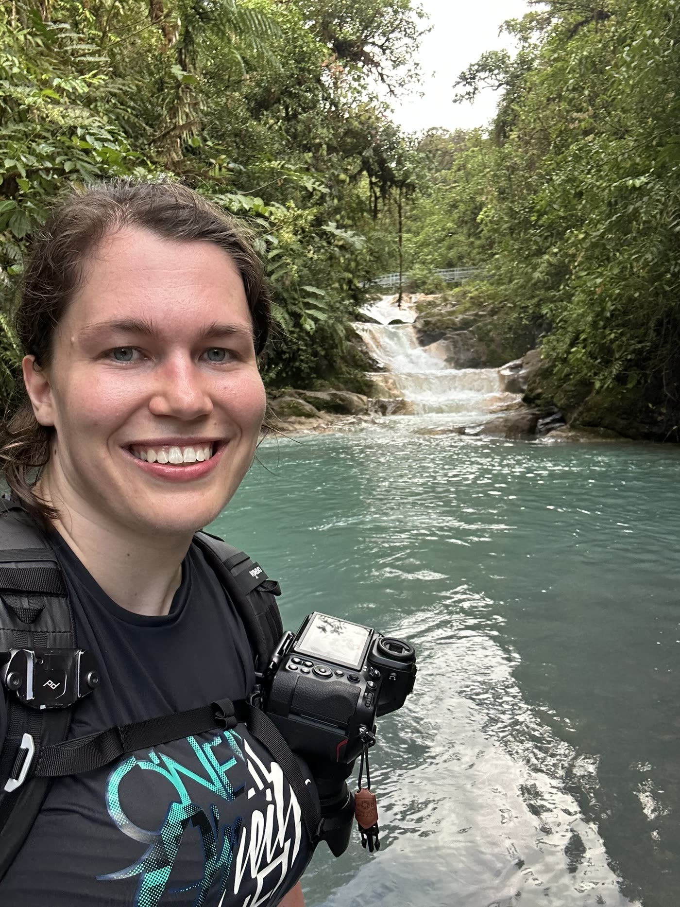 Janet mit Kamera an einem türkisfarbenen Fluss.