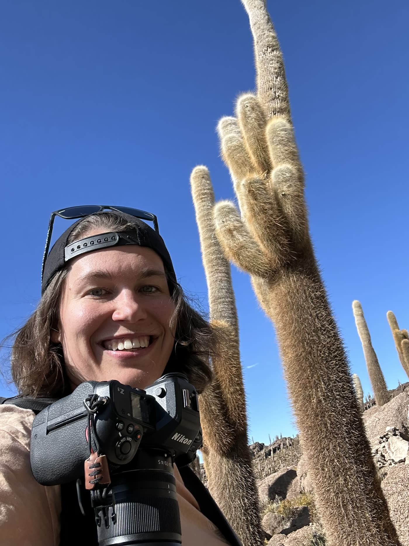 Janet mit Kamera vor großen Kakteen und blauem Himmel.