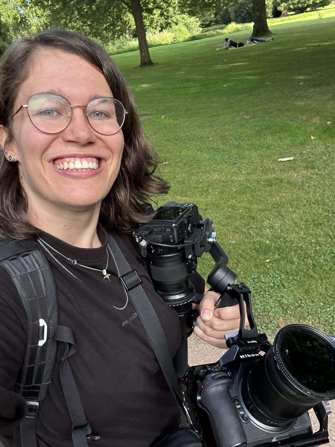 Janet fotografiert sich selbst mit zwei Kameras im Grünen.