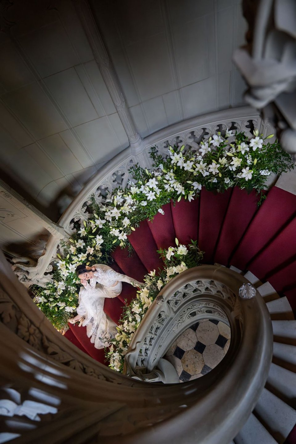 Ein Paar liegt auf einer mit Blumen geschmückten Wendeltreppe, von oben fotografiert.