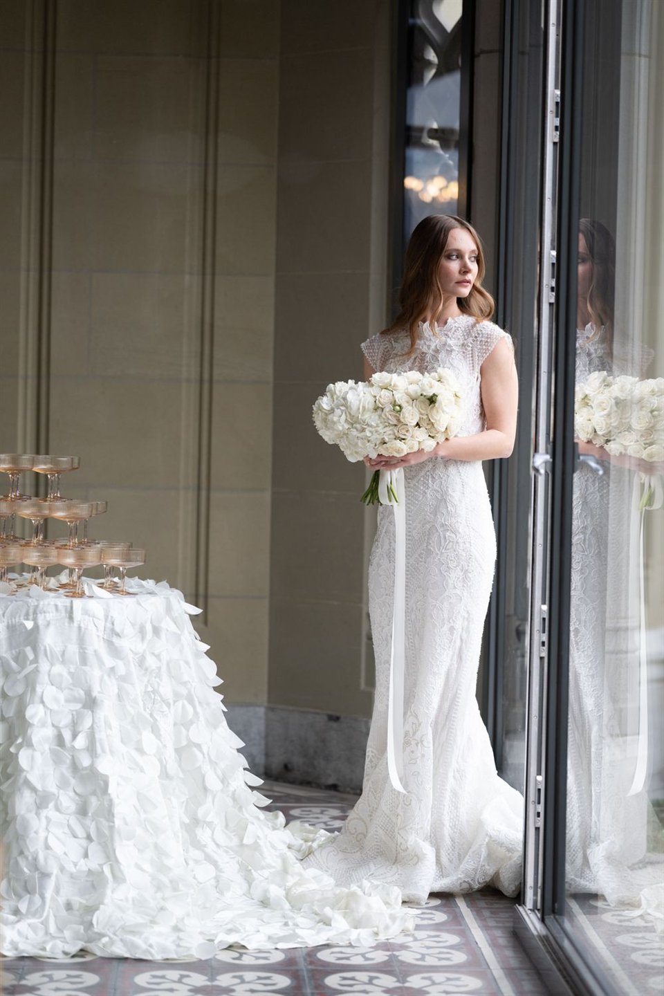 Eine Person mit Blumen im Hochzeitskleid am Fenster.