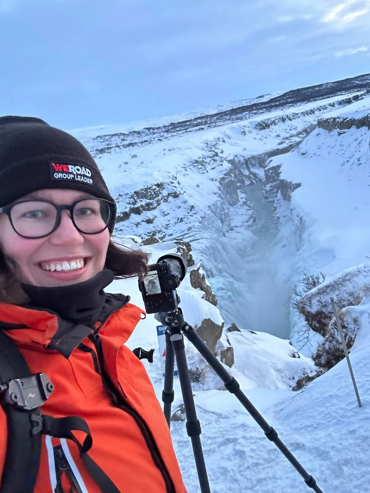 Janet with a camera and tripod in front of a snow covered gorge.