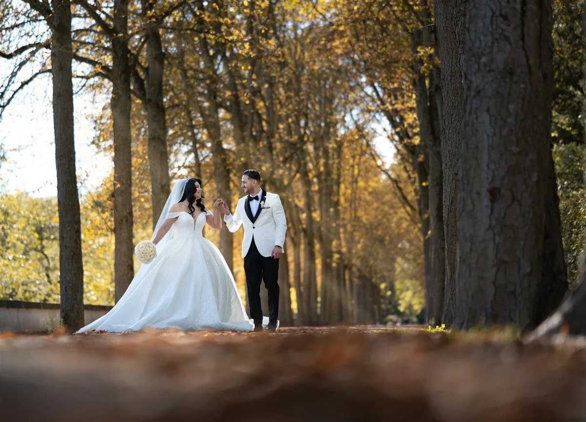 A couple walk hand in hand through an autumn avenue of trees.