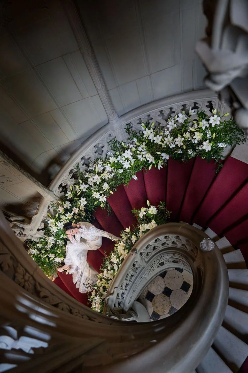 A couple lie on a flower decorated spiral staircase, photographed from above.