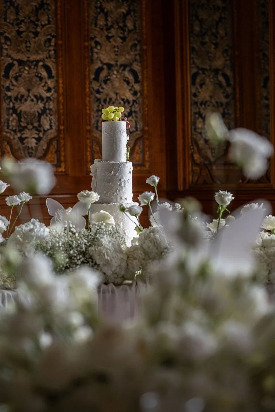 A white wedding cake among densely arranged white flowers.
