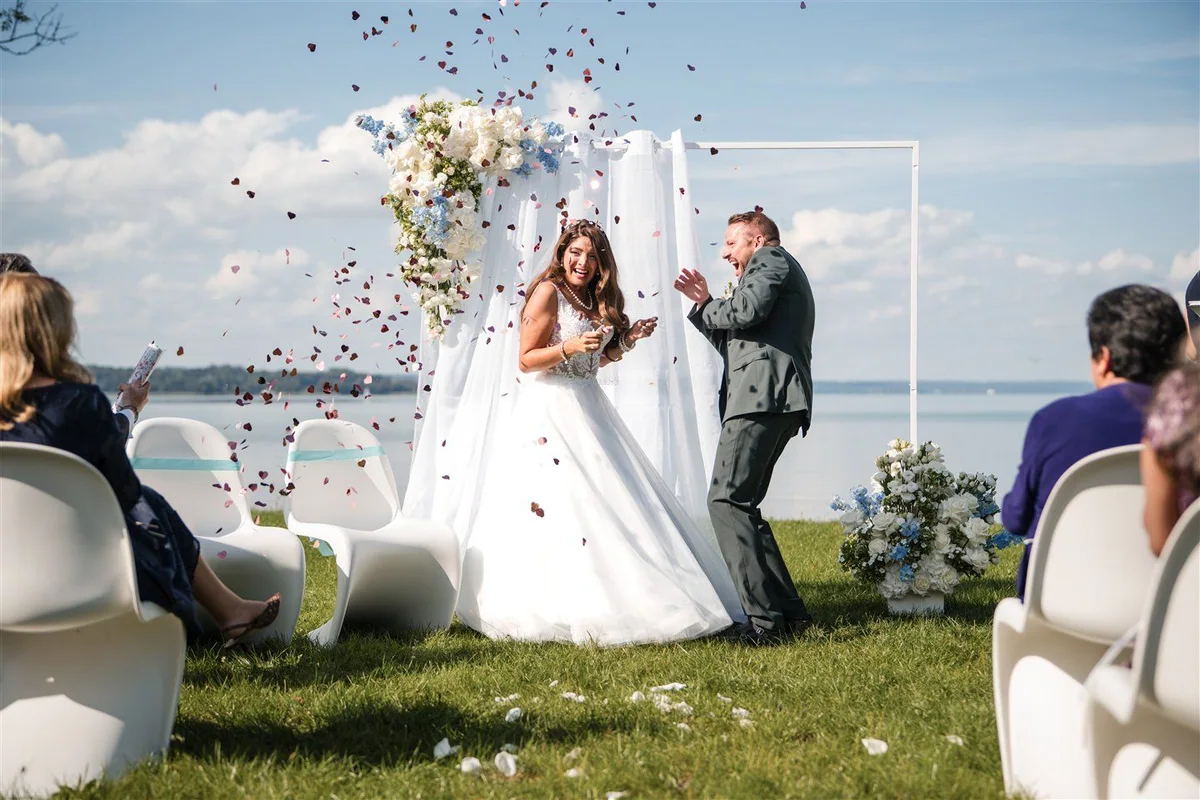 Guests throw flower petals over a couple by the lake.