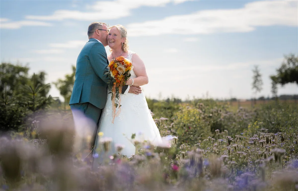 A couple laugh together in a meadow full of wildflowers.