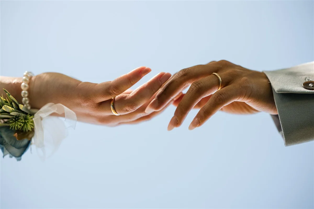 Two hands with wedding rings against the sky.