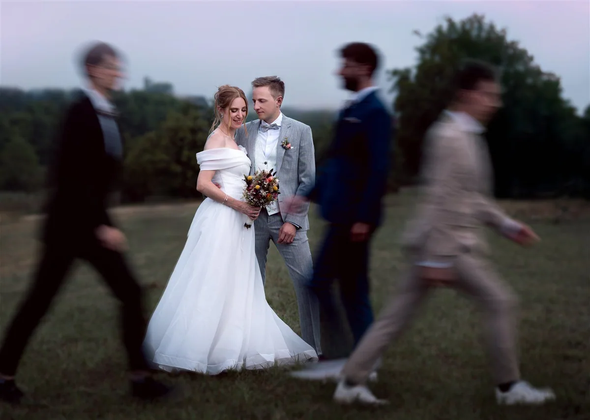 A couple stand quietly together as guests pass out of focus.