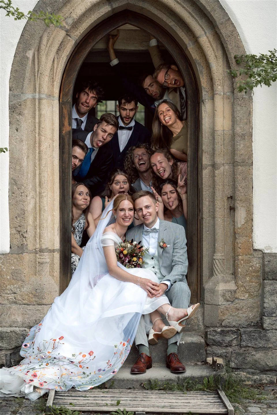 Guests crowd laughing behind the couple in a church doorway.