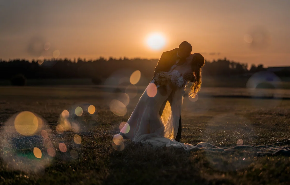 A wedding couple kiss in a field in deep evening light.
