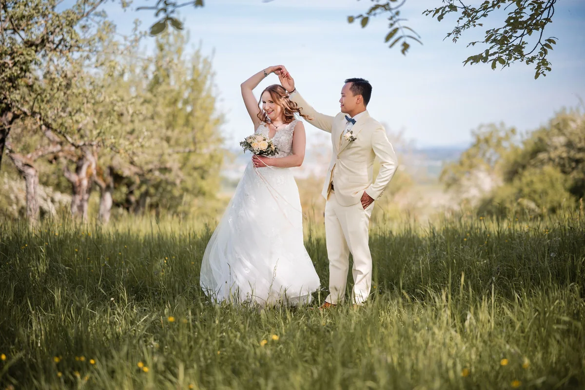 A wedding couple spin hand in hand on a green meadow.