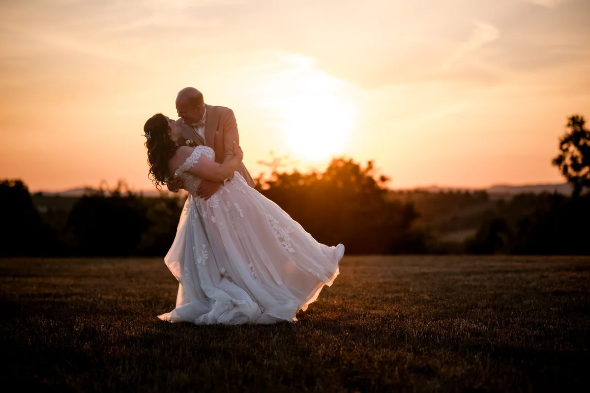 A bride is carried in someone’s arms at sunset.