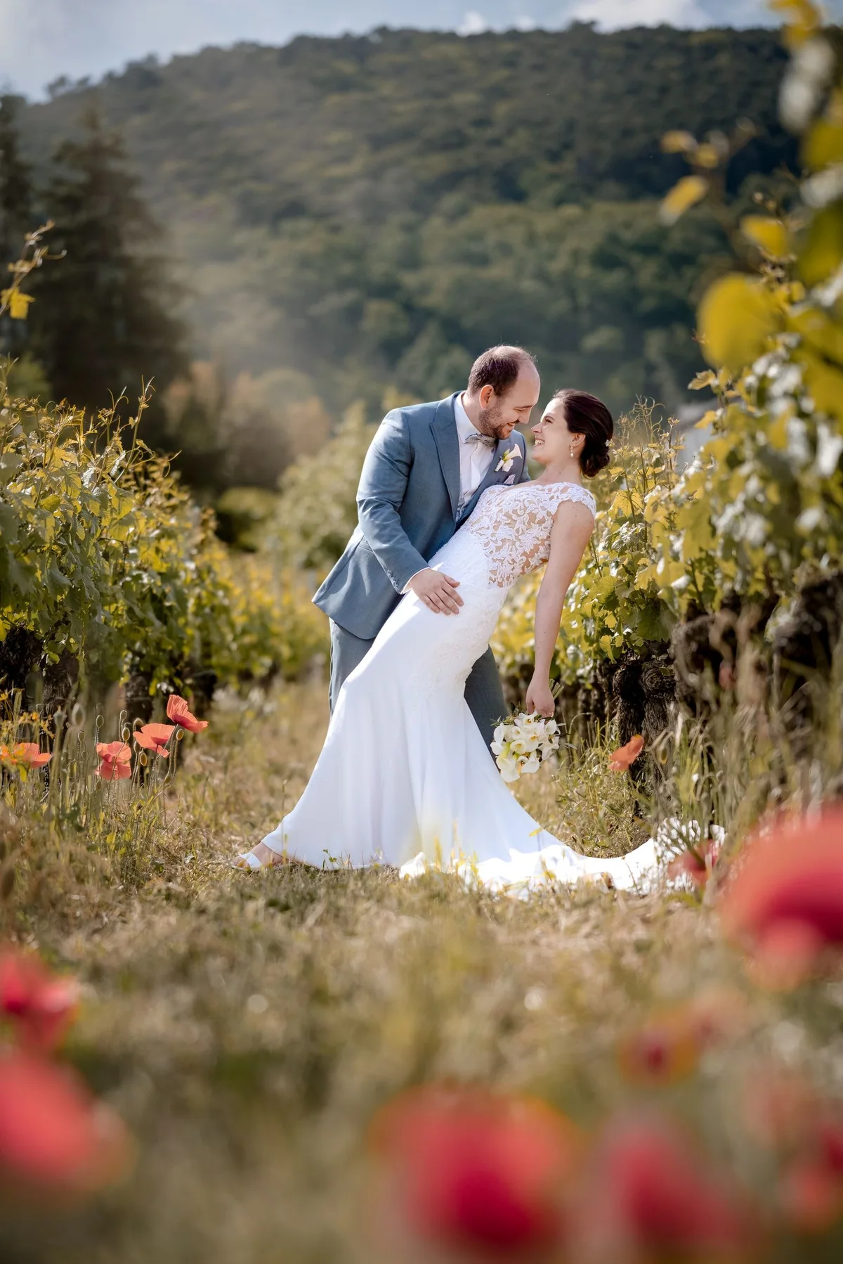 A wedding couple kiss among flowers with mountains behind them.