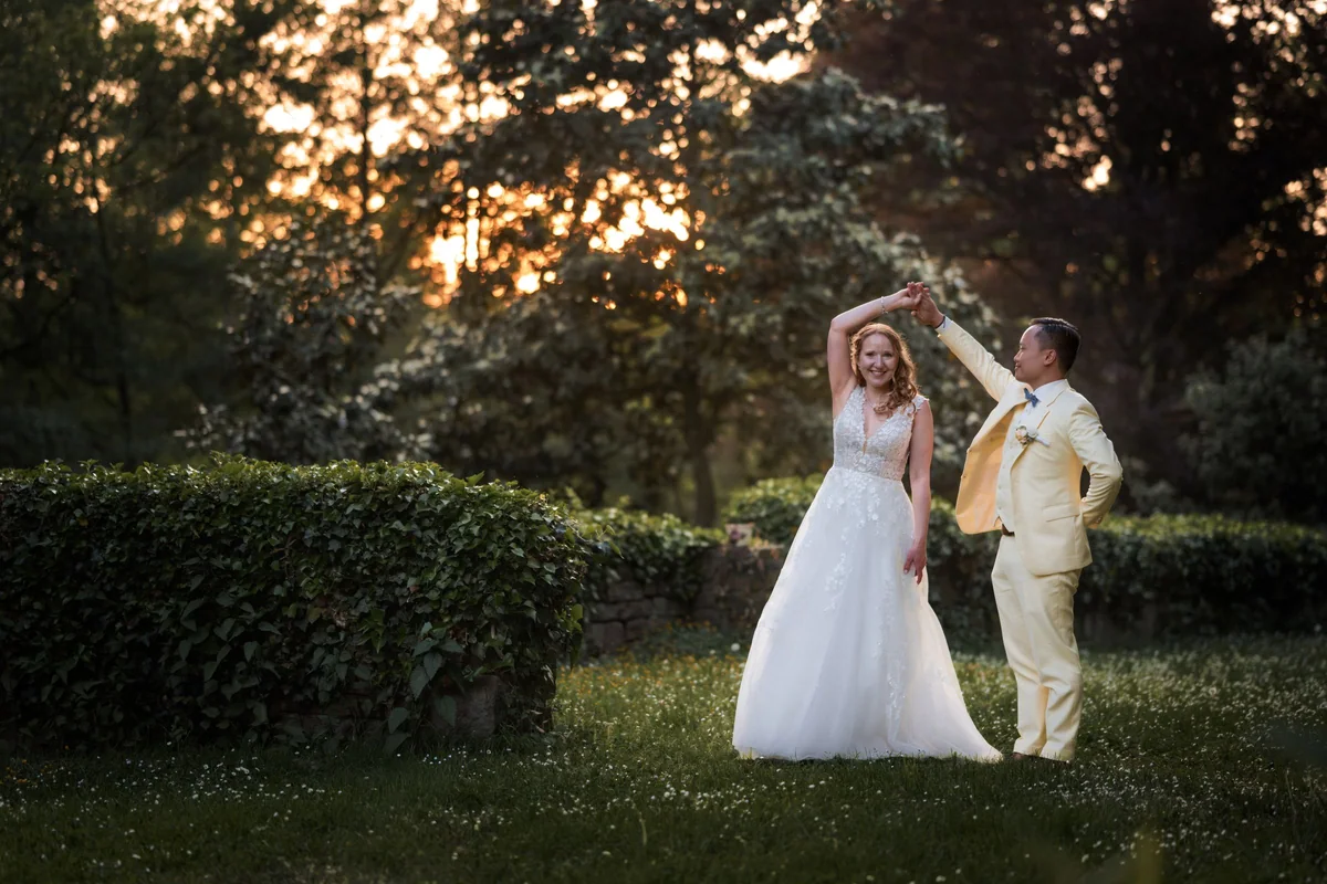 A wedding couple stand beneath a tree in warm backlight.