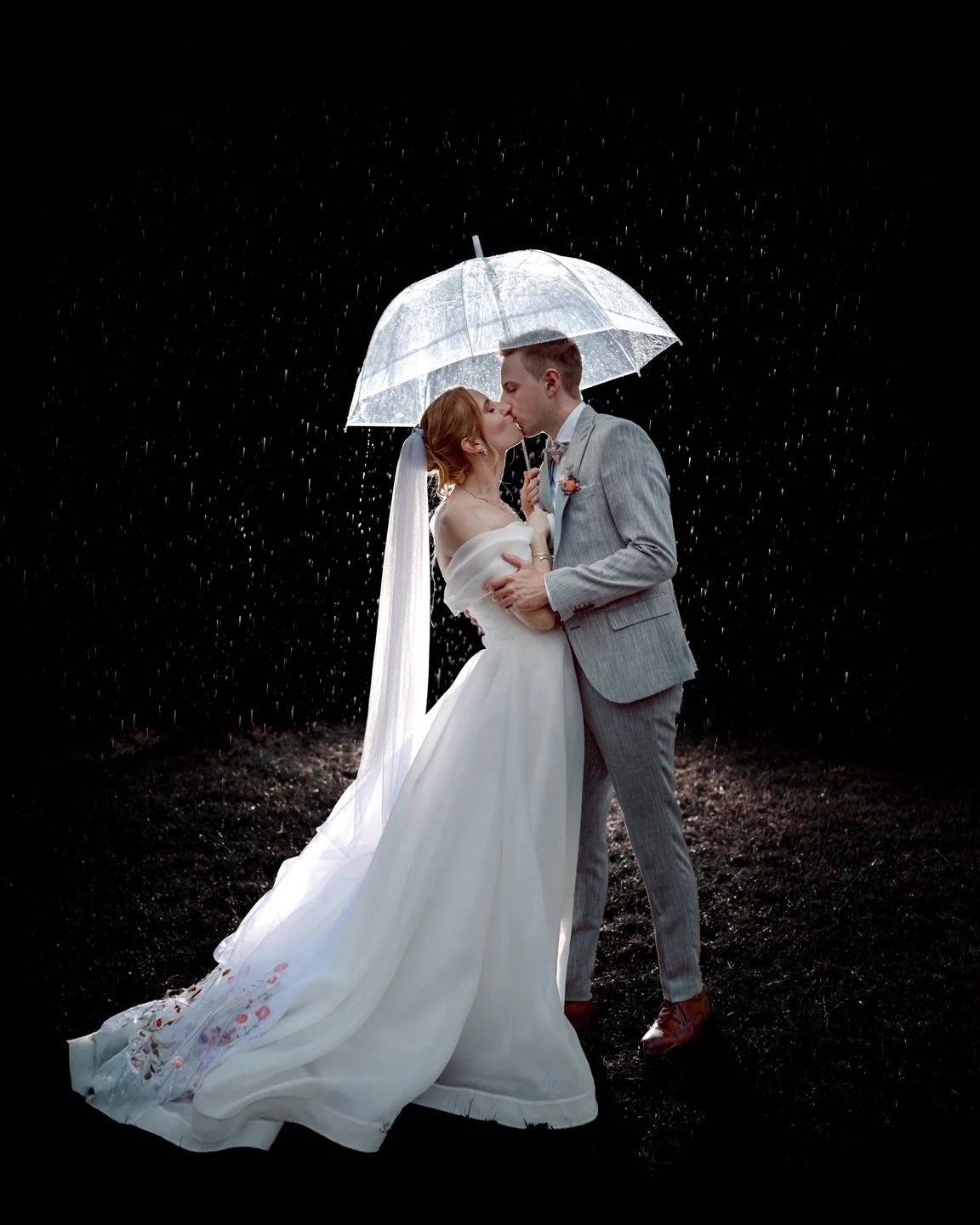 A couple kiss at night beneath a clear umbrella, with raindrops lit by a flash.