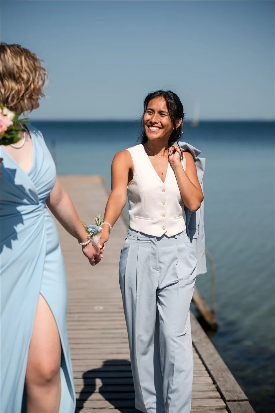 The couple laugh on a jetty by the water.