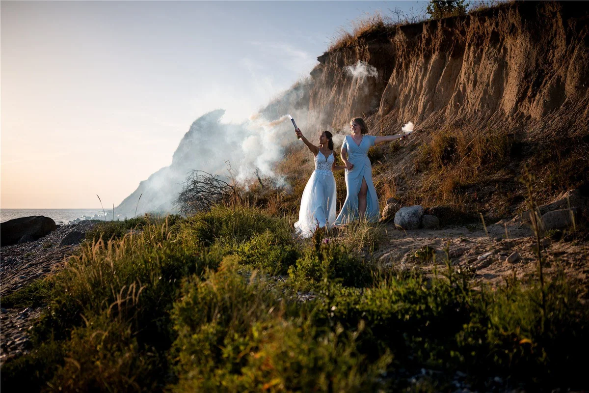 Two people in front of a sea cliff with smoke rising beside them.