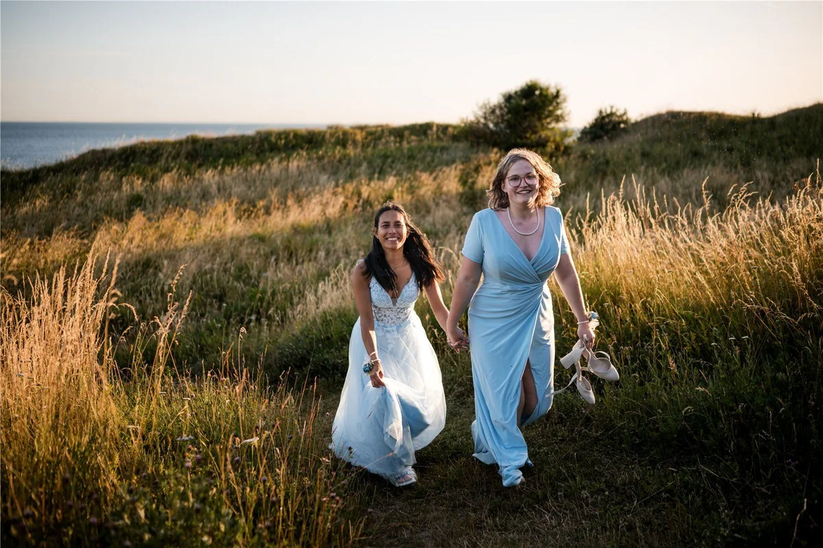 The couple walk hand in hand through a meadow.