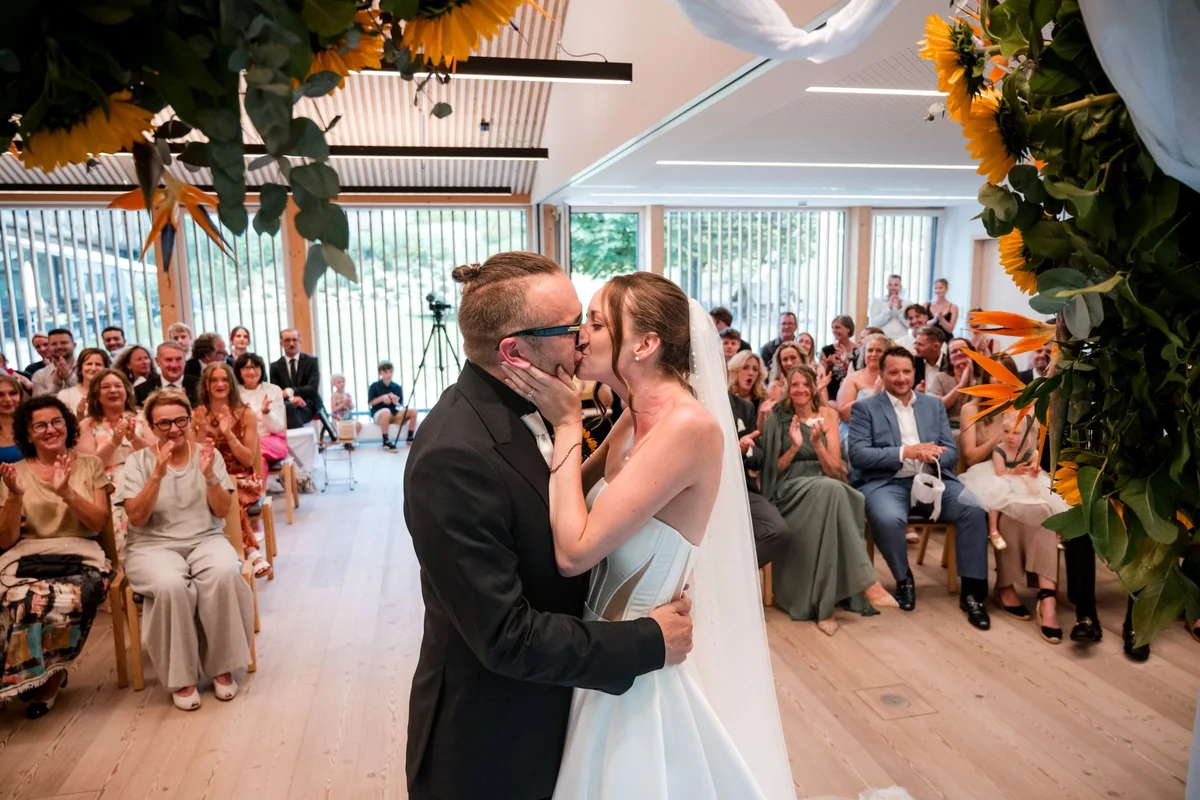 The wedding couple kiss during the ceremony beneath the sunflower arch.
