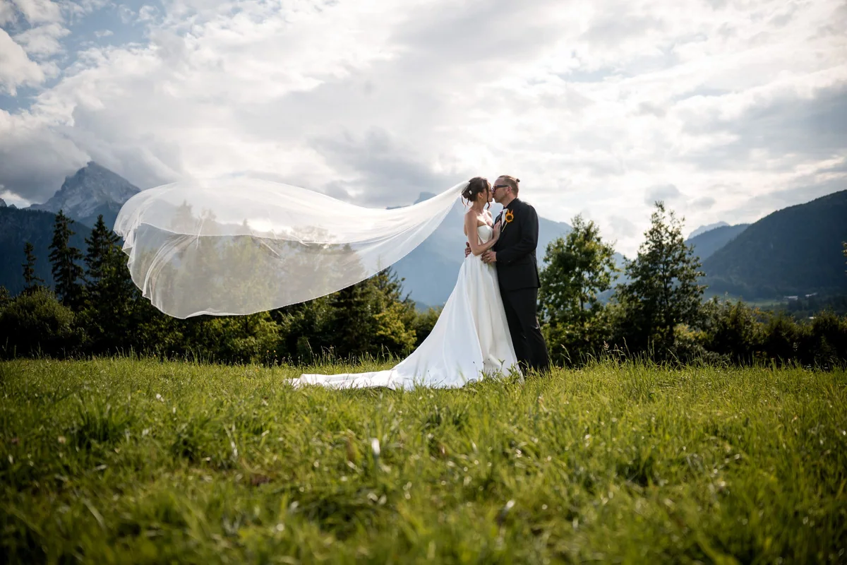 A kiss with a flowing veil in front of the mountains.
