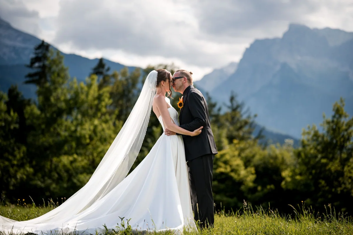 The wedding couple kiss in sunlight with mountains behind them.