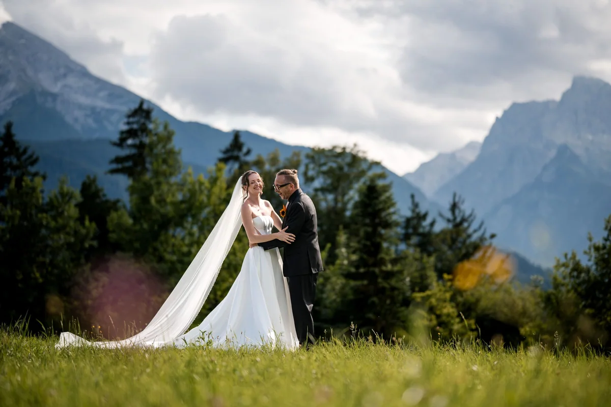 Brianna and her husband stand in a mountain meadow with her long veil.