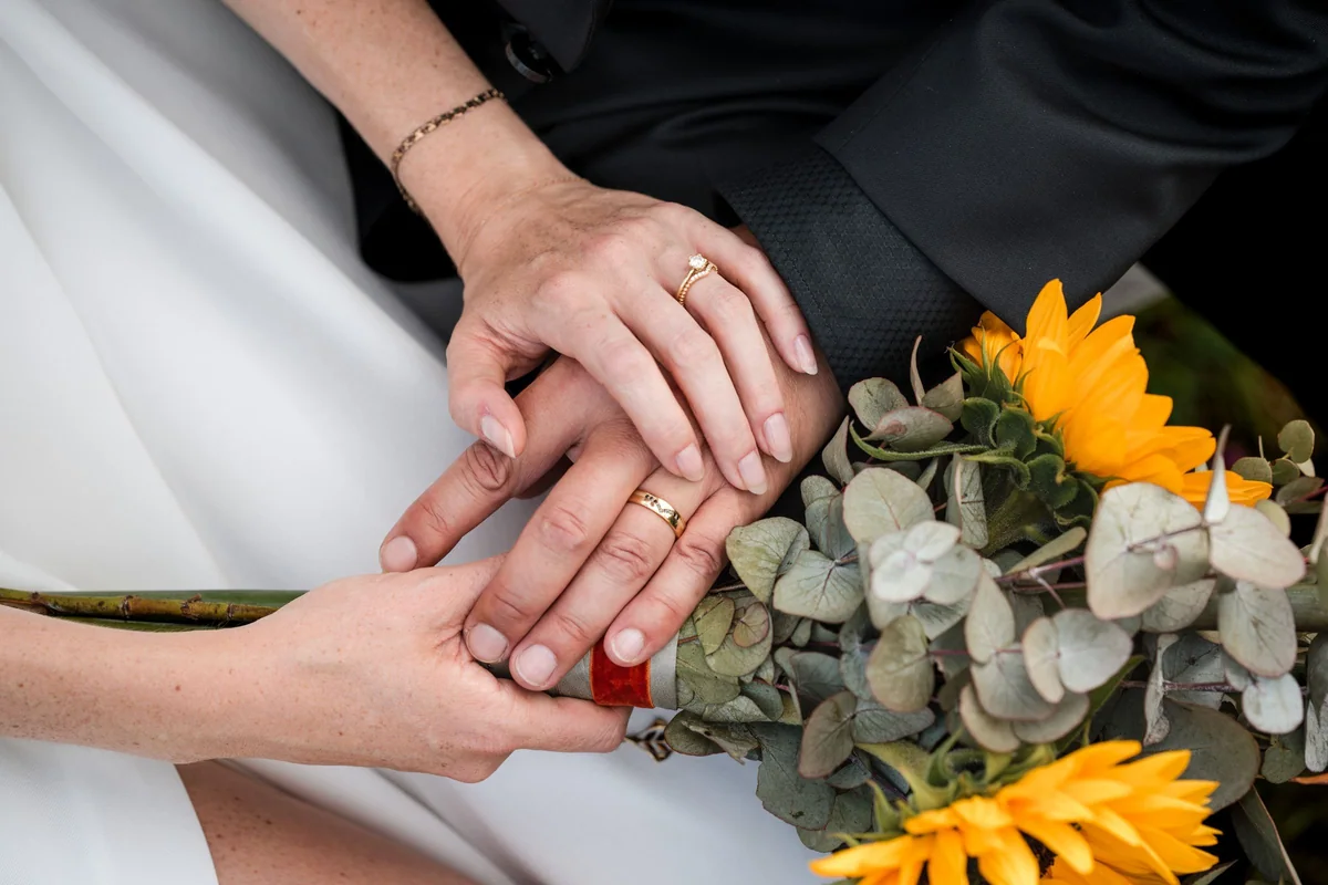 Hands with wedding rings beside a sunflower bouquet.