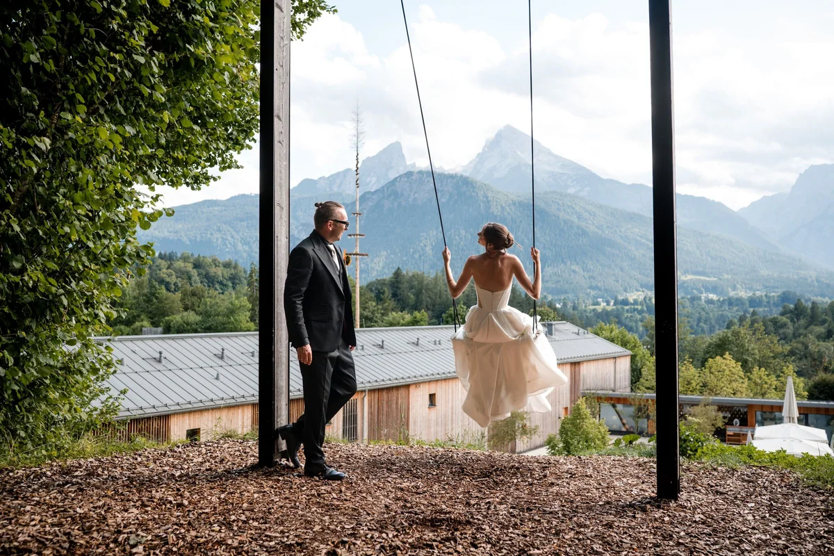 The wedding couple by a swing in front of the mountain landscape.