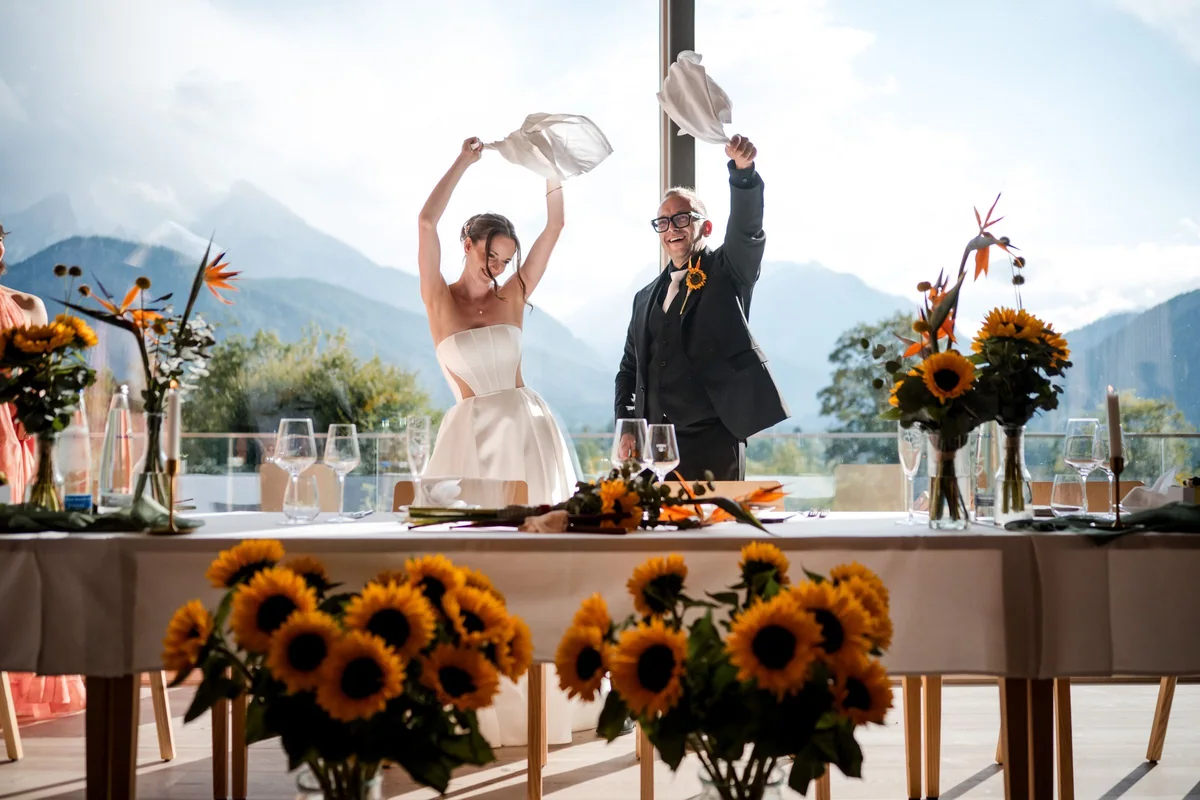 The wedding couple wave napkins behind a table decorated with sunflowers.