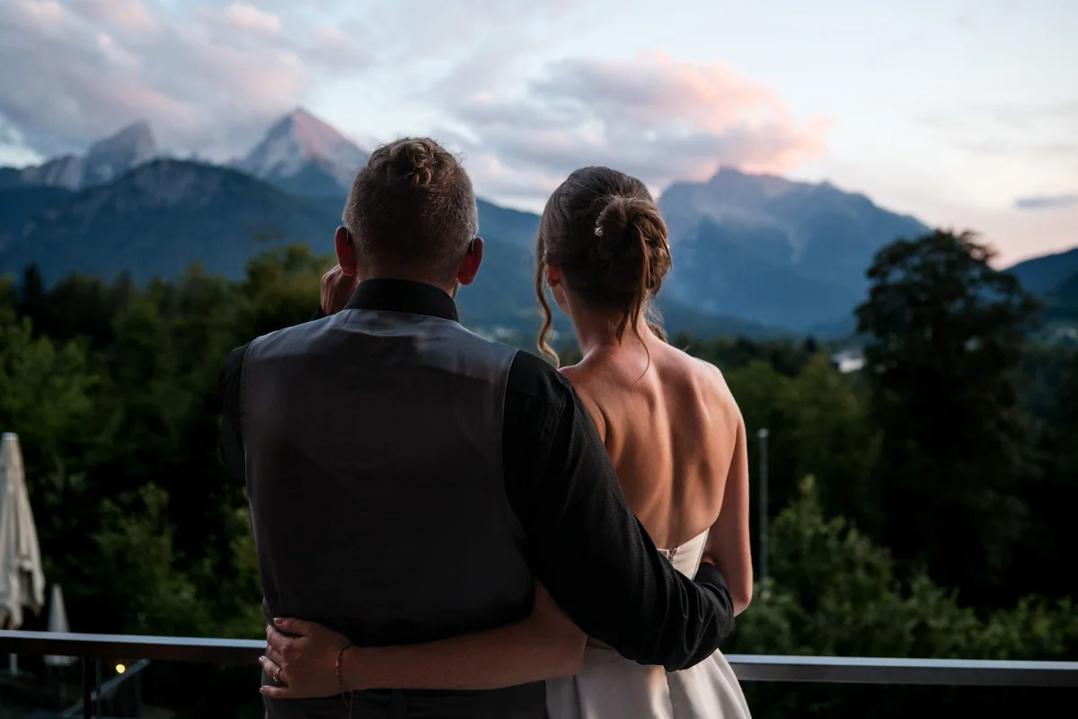 The wedding couple look at the mountains together in the evening light.
