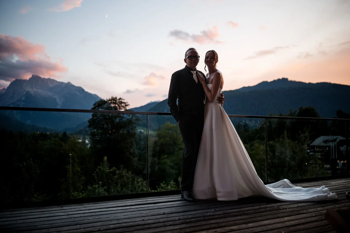 The wedding couple in front of mountains and a pink evening sky.