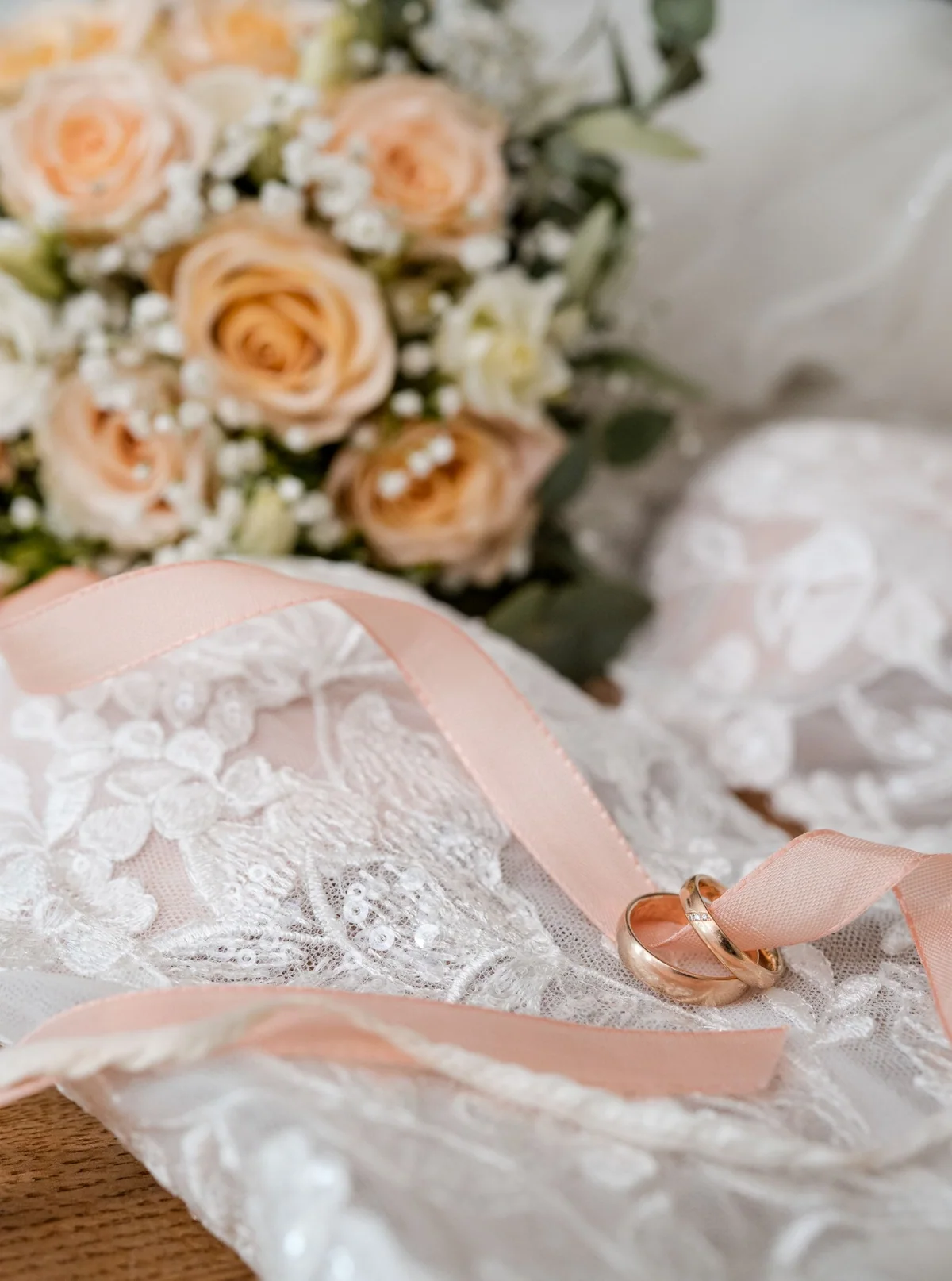 Die Eheringe liegen auf der Spitze des Brautkleids, daneben ein Band in Apricot und der Strauß aus Rosen.
