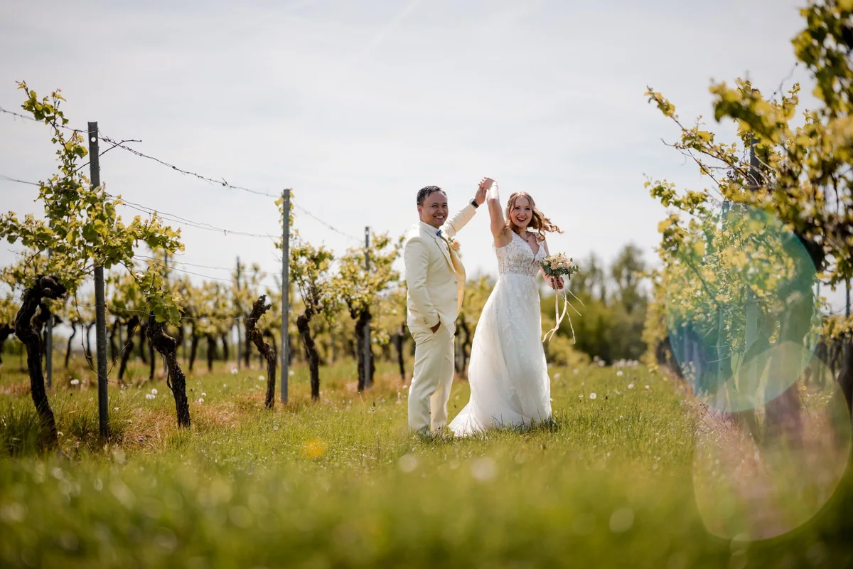 Between the rows of vines the groom twirls the laughing bride by the hand.