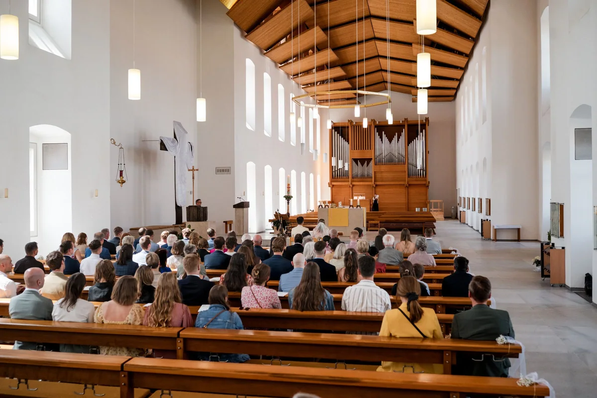 View from the back of the large, bright church with its wooden ceiling and organ, guests seated in the pews.