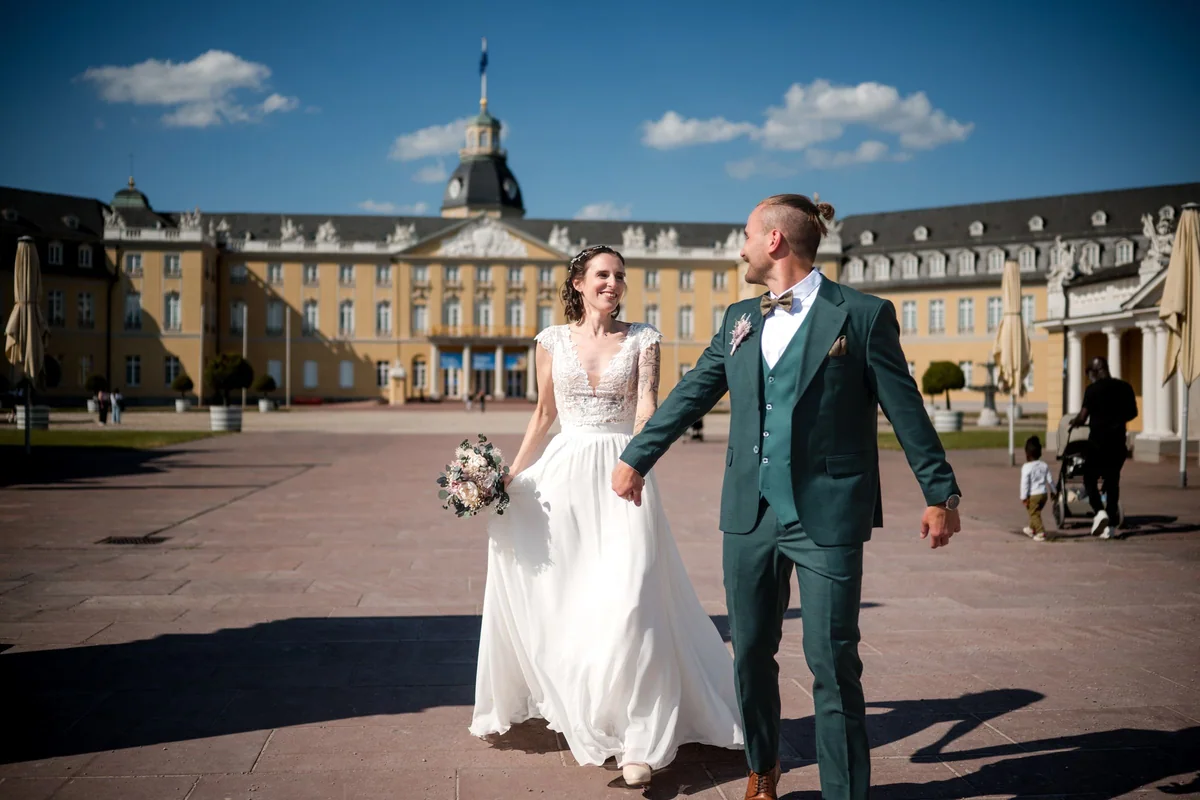 Das Brautpaar geht Hand in Hand über den Platz vor dem Karlsruher Schloss.