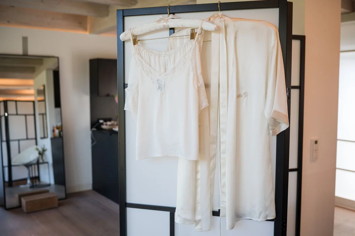 Das Hochzeitskleid hängt vor einer hellen Trennwand bereit.