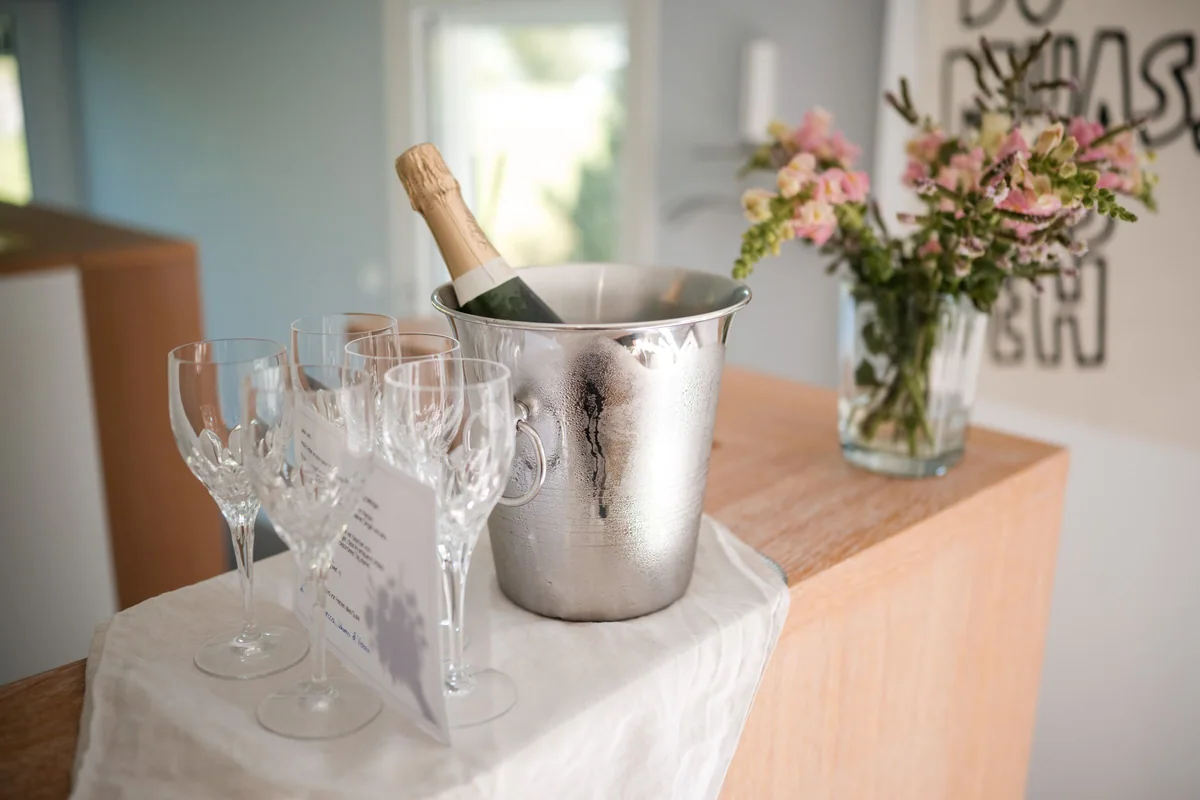 Sektgläser stehen neben einer Flasche im Kühler und einer Blumenvase bereit.