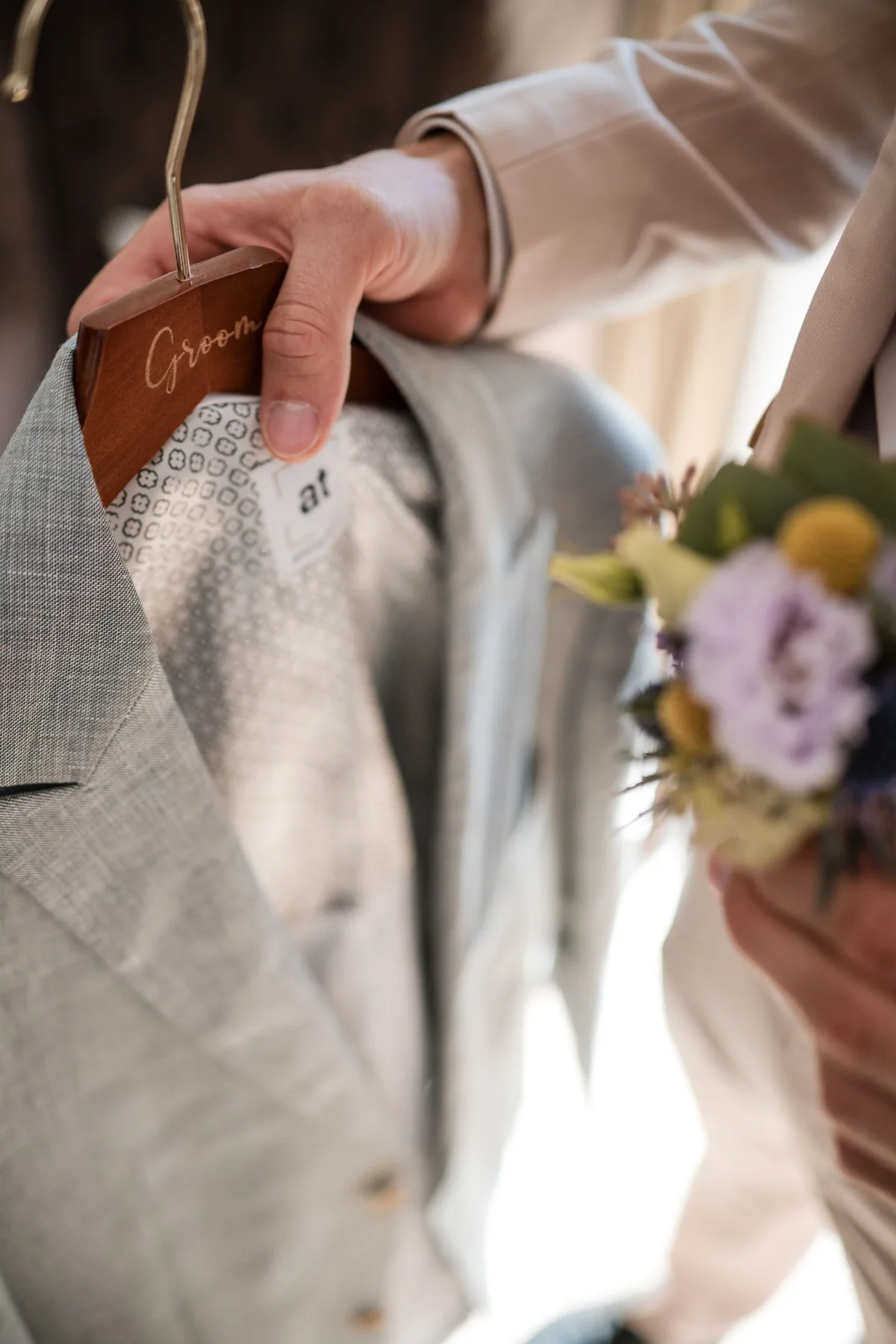 Eine Hand richtet den Stoff am hellgrauen Hochzeitsanzug.