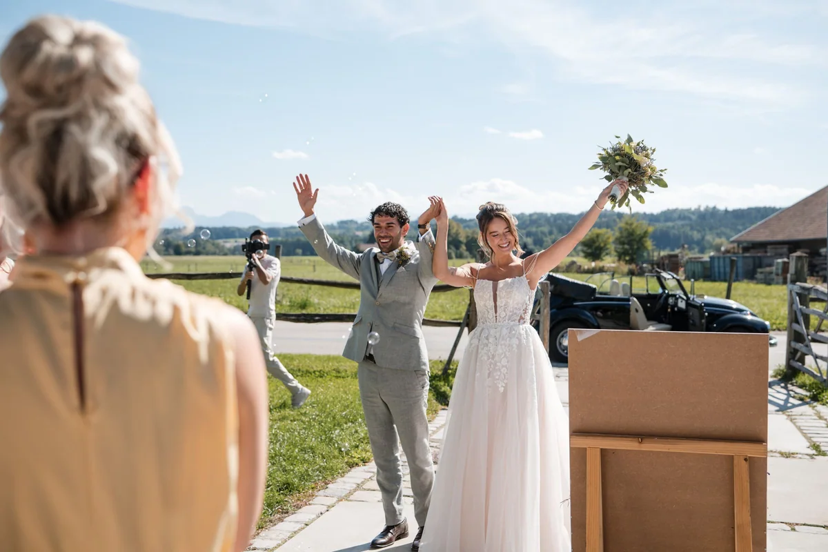 Leah und Sina begrüßen ihre Gäste mit erhobenen Armen im Freien.