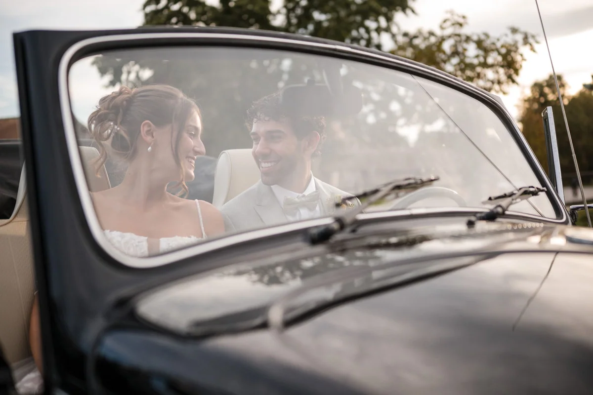Leah und Sina lachen auf den Vordersitzen eines offenen Oldtimers.