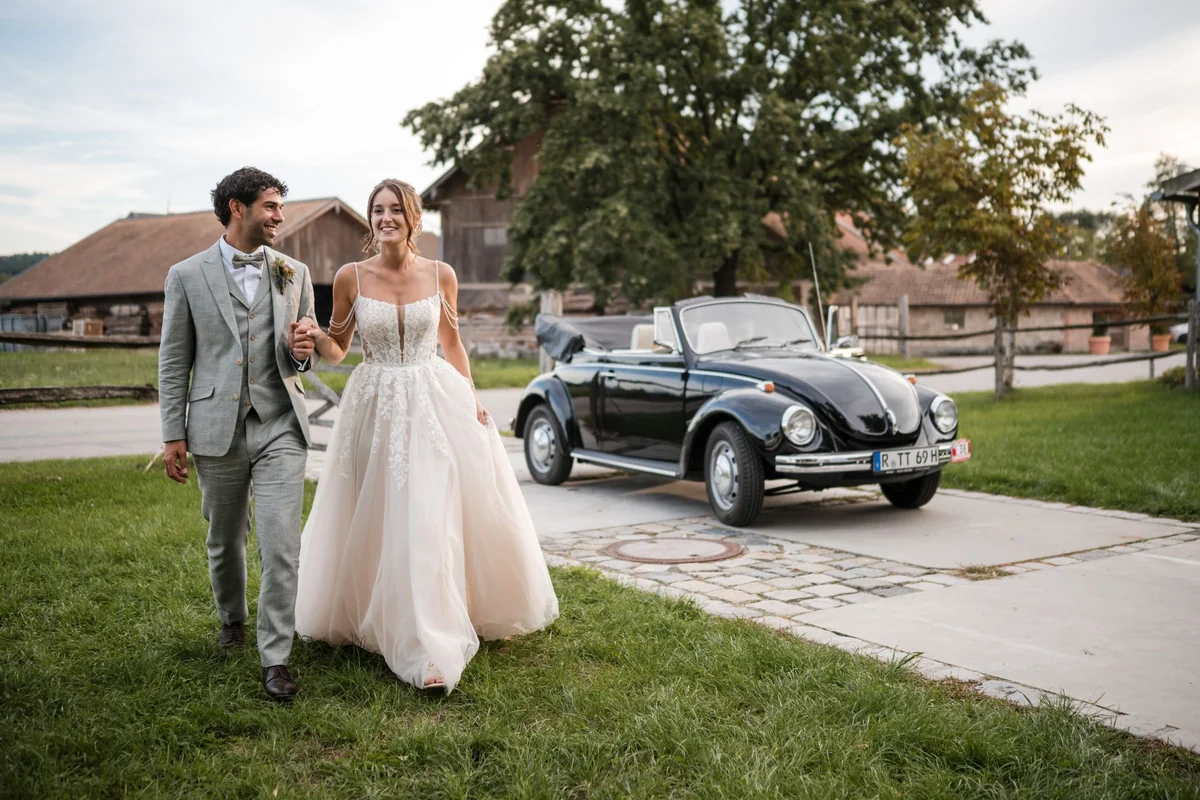 Leah und Sina gehen Hand in Hand vor dem schwarzen Oldtimer.
