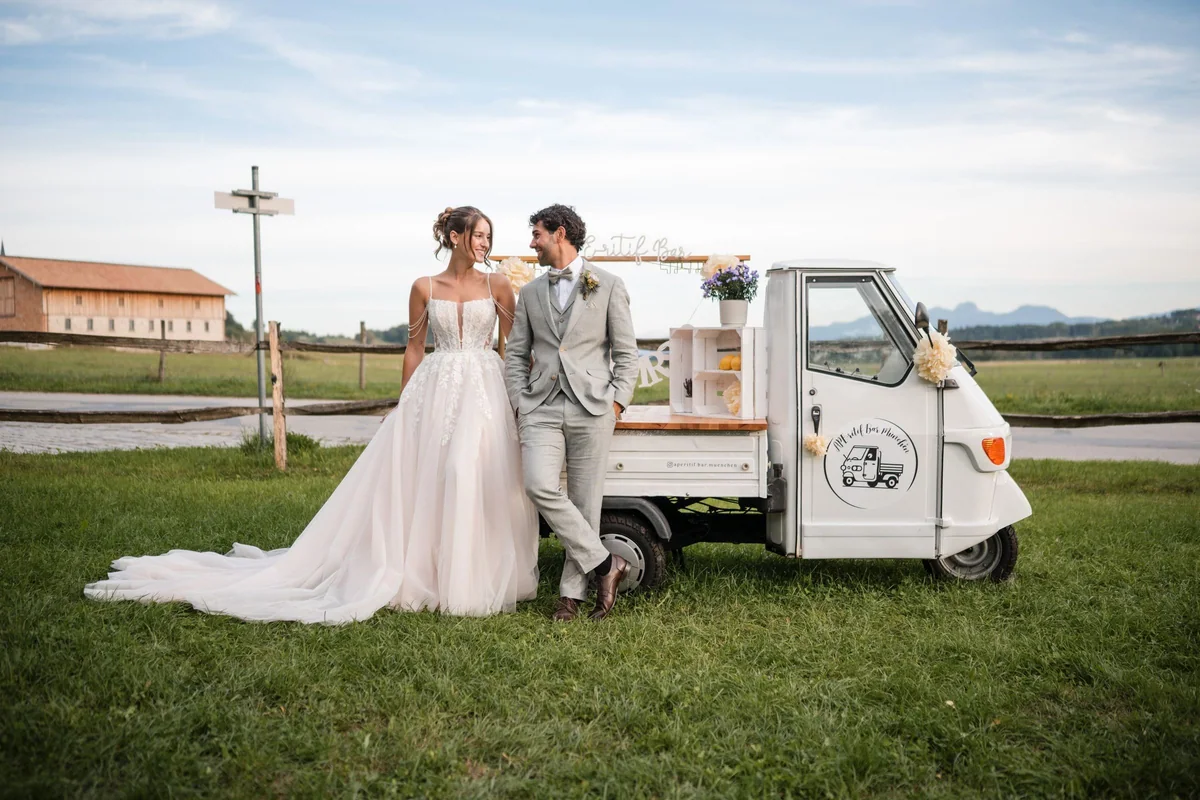 Leah und Sina stehen neben ihrer weißen Ape mit geöffneter Seite und Holzdetails auf der Wiese.