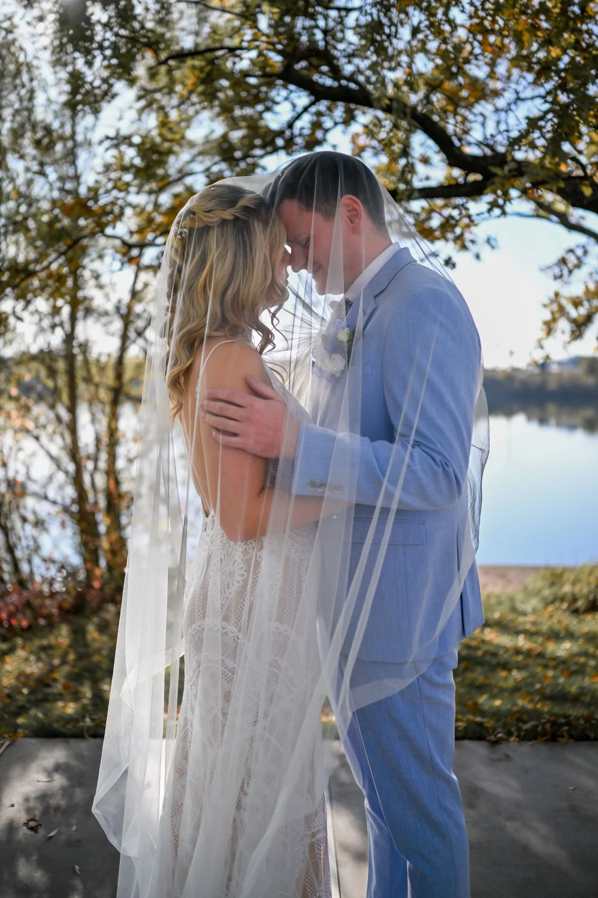 Beneath the veil the couple kiss on the shore, the lake behind them.