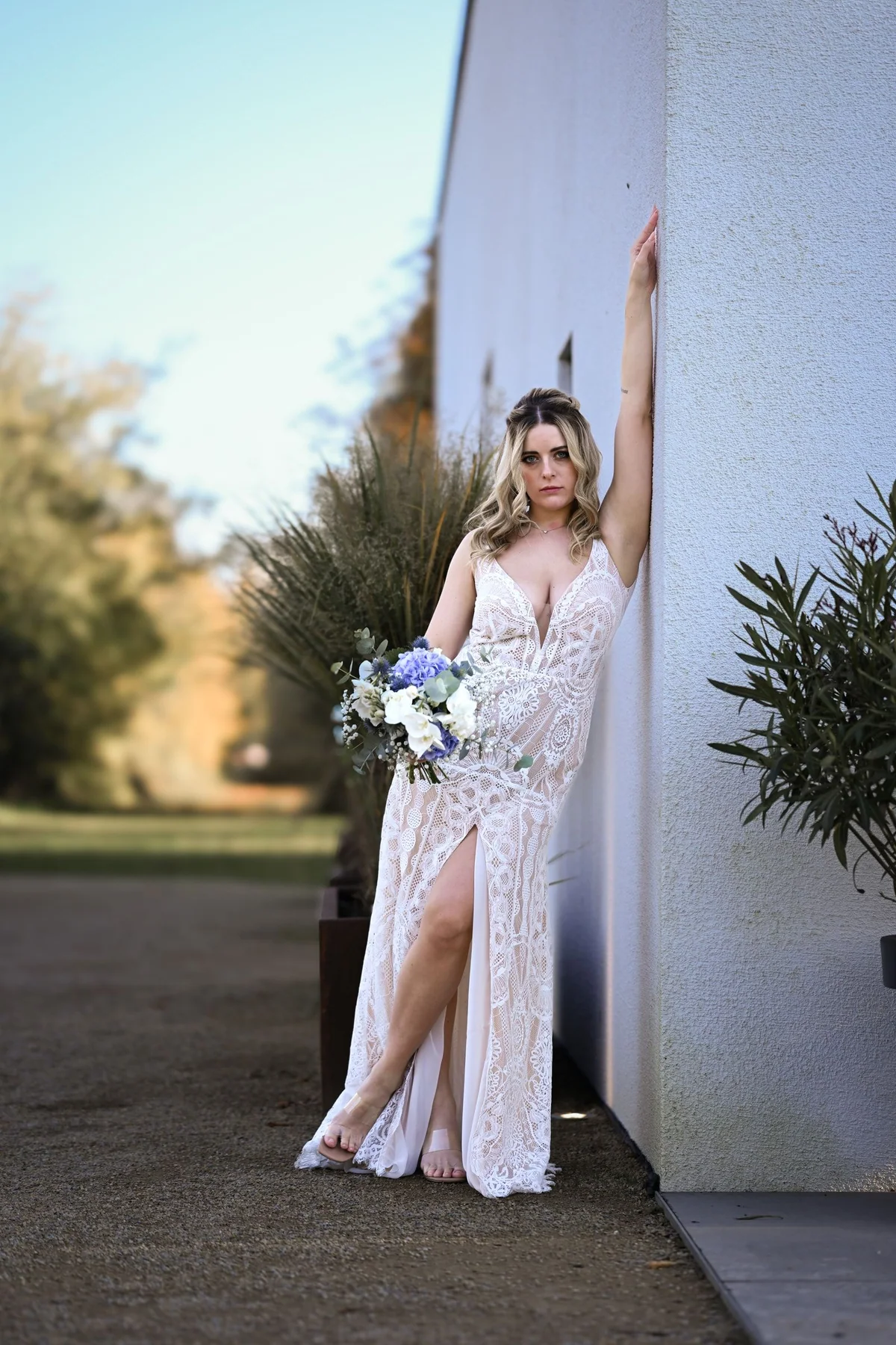 The bride leans against the white façade of the Seehaus with her bouquet, one arm raised against the wall.