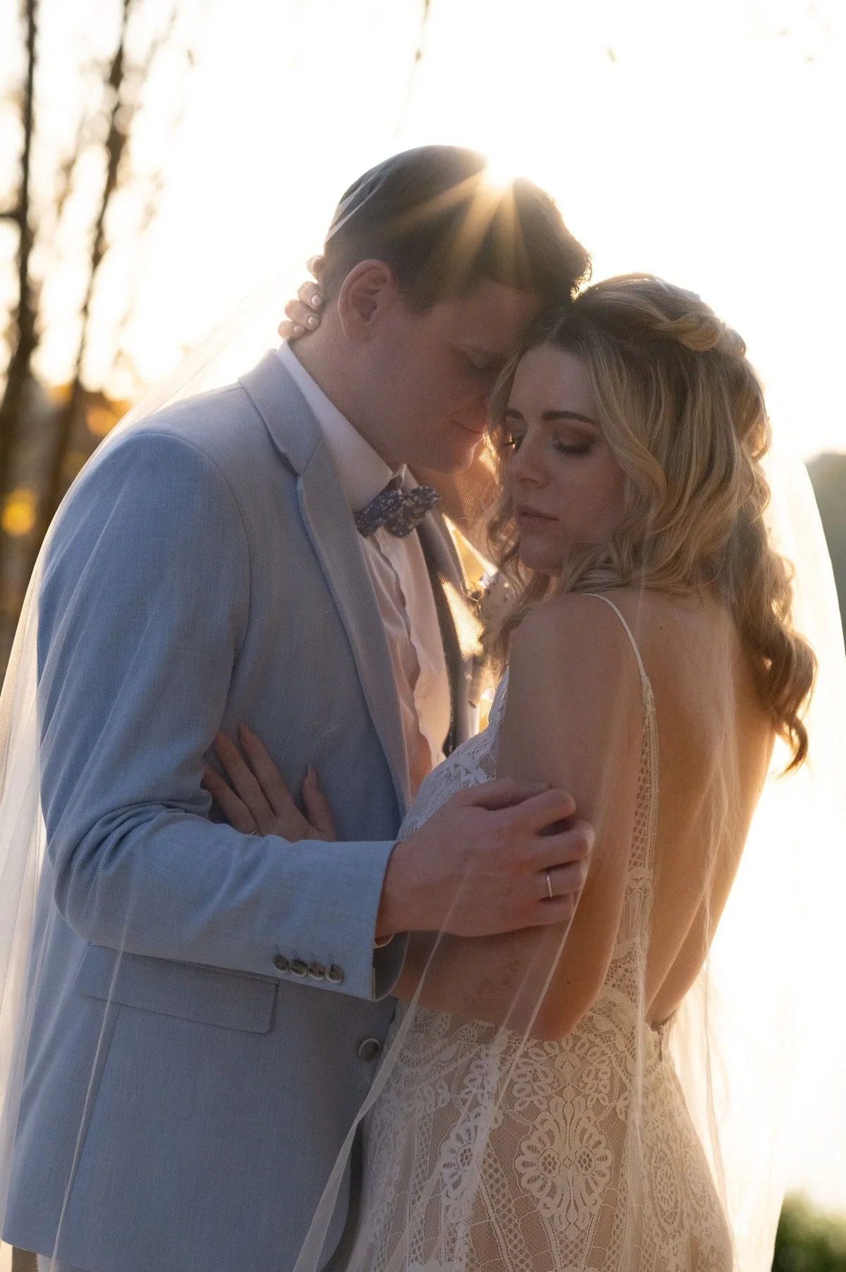 A couple leans forehead to forehead in backlight by the lake.