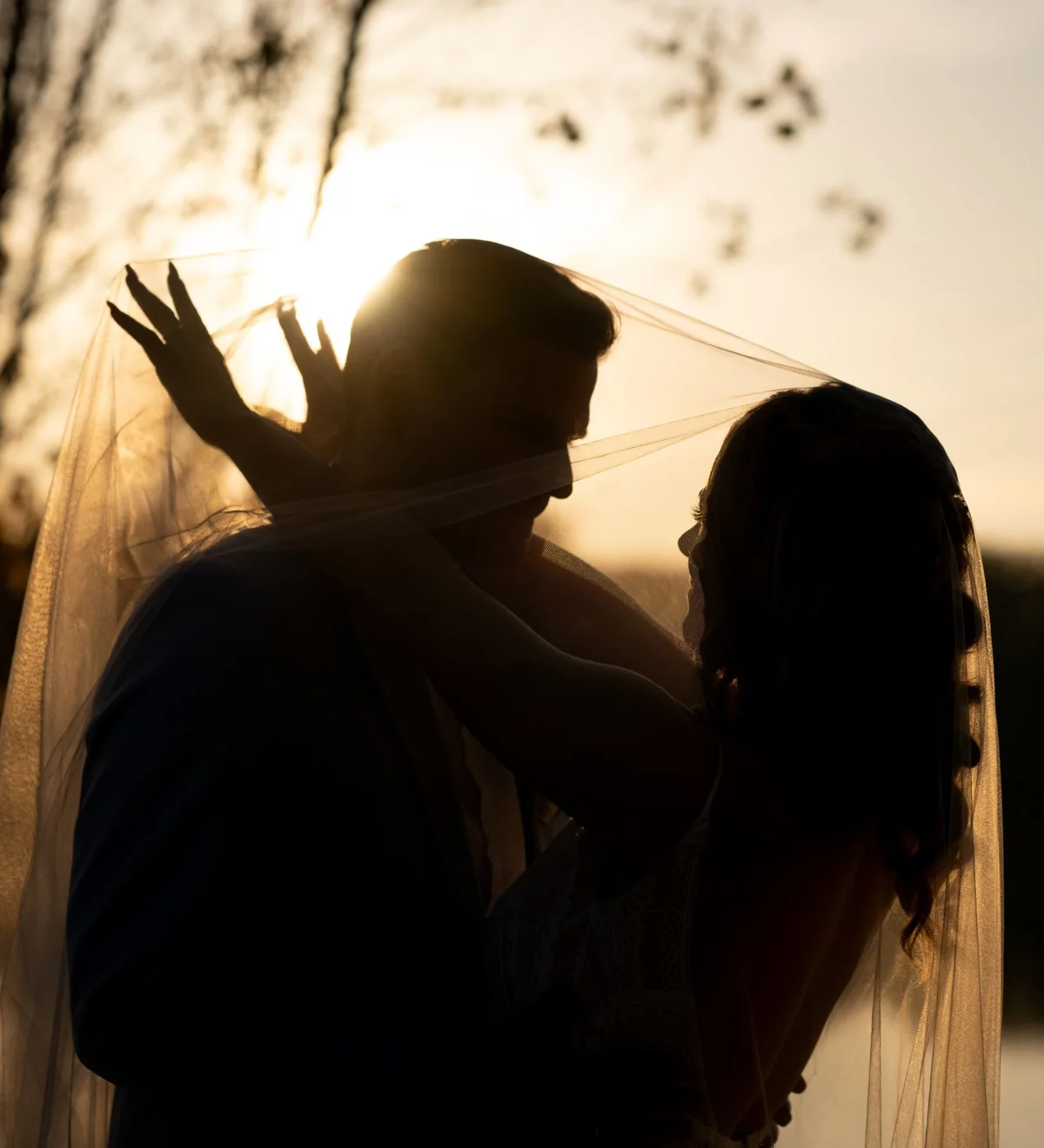 The silhouettes of the couple beneath the veil against the setting sun.