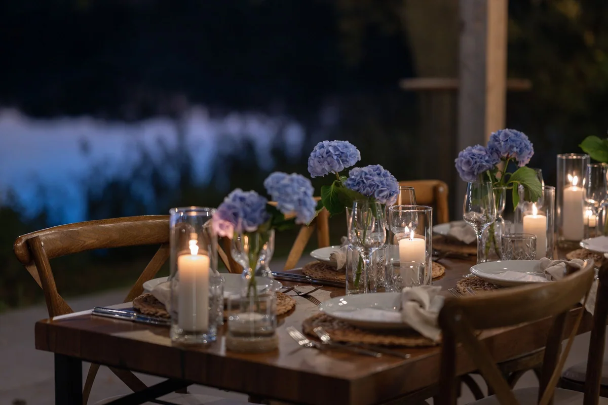 The laid table with candles and blue hydrangeas in the evening, the lake behind.