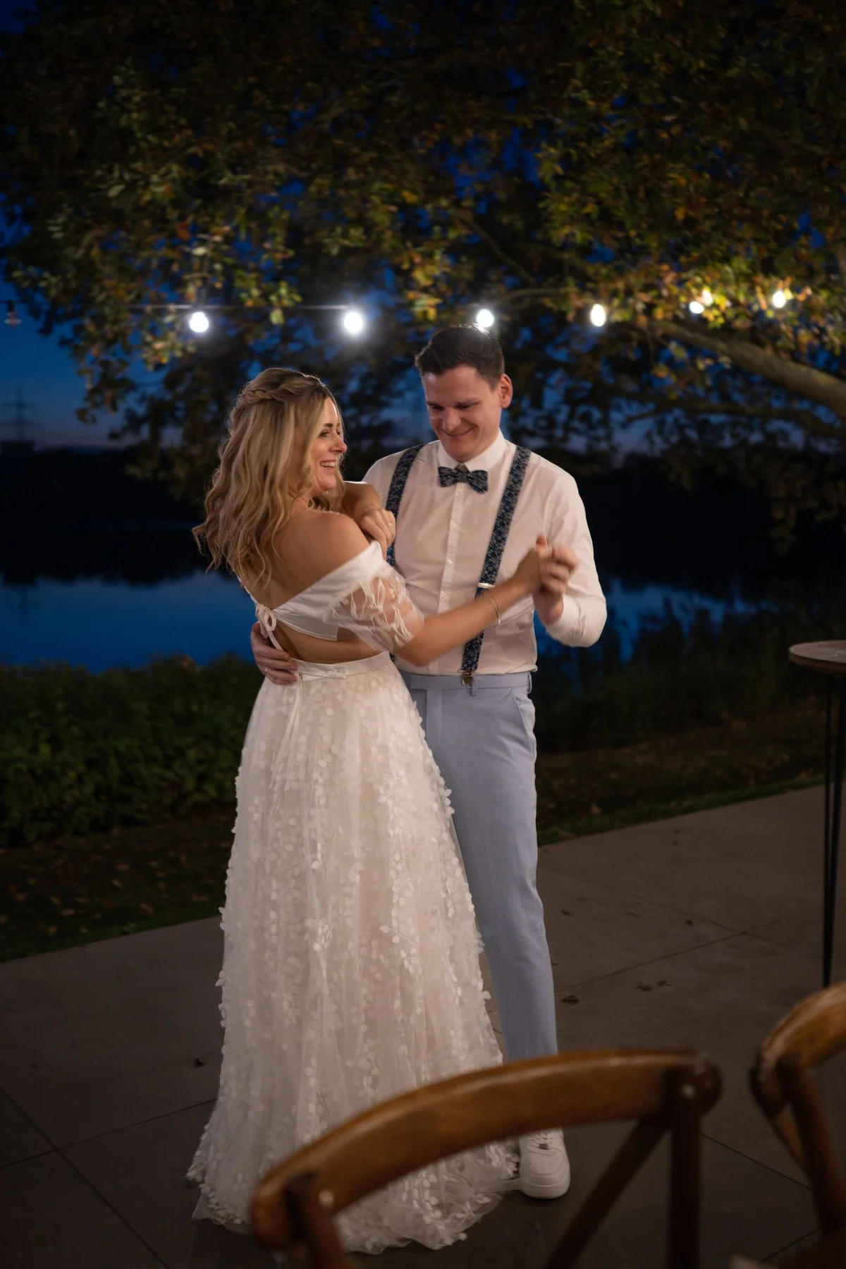The couple dance on the terrace in the evening beneath strings of lights.